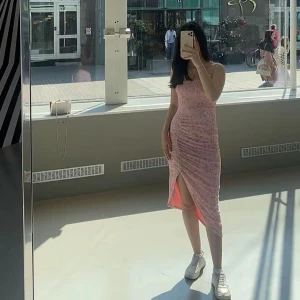 Rosa blommig omlottklänning - Säljer en söt rosa klänning med blommigt mönster och omlott-detalj. Klänningen har smala axelband, slits framtill och en figurnära passform som framhäver siluetten. Perfekt för varma dagar och somriga vibes.