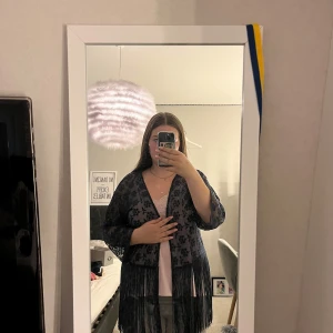 Blå spets kofta med fransar från H&M - Säljer en marinblå volang kofta från H&M med blommigt spetsmönster och långa fransar nedtill. Koftan är transparent, har trekvartsärmar och öppen front. Perfekt för att ge outfiten en extra touch med coola detaljer.