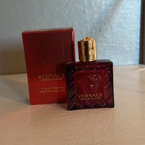 Versace Eros Flame parfym 5ml - Versace Eros Flame Eau de Parfum i en lyxig röd miniflaska med guldigt lock. Flaskan har Versaces ikoniska Medusa-mönster och kommer i matchande röd kartong. Perfekt storlek för att ta med sig och en riktigt snygg detalj på hyllan.