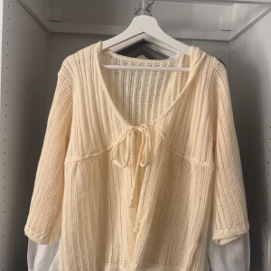 Beige stickad kofta med knyt - Superfin beige stickad kofta med ribbad struktur och v-ringning. Koftan har knyt framtill och trekvartsärmar, perfekt för lager-på-lager och en chill vibe. Passar snyggt till både jeans och kjol.