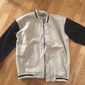 Beige/svart jacka Gina Tricot - Jacka från Gina Tricot i beige med svarta ärmar och detaljer. Jackan har tryckknappar, randiga muddar och texten 'AUTHENTIC' på ryggen. Använd 1-2 gånger. Den är lagomt tunt/tjock, perfekt för hösten. Pris kan diskuteras! 