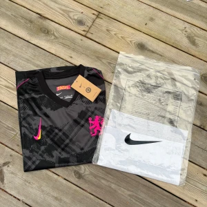 Chelsea fotbollströja  - Snygg fotbollströja från Nike i svart och grått med grafiskt mönster, korta ärmar och coola neonrosa detaljer. Broderad rosa lejonlogga på bröstet och gul/rosa Nike swoosh. Materialet är lätt och andas, perfekt för match eller träning.Pris kan diskuteras vid snabb affär 