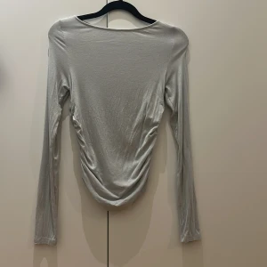 Ljusgrå långärmad topp med rynk - Säljer en ljusgrå/beige långärmad topp med snygga rynkade detaljer längs sidorna. Modellen har en smal passform och är i ett mjukt och stretchigt material. Skulle säga att den passar storlek xs/s
