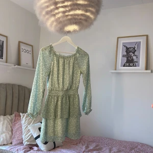 Ljusgrön blommig klänning KappAhl - Använd 1 gg ( skolavslutningen).   Supersöt ljusgrön kortklänning från KappAhl med små vita blommor, långa ärmar och volangkjol. Klänningen har smock i midjan och är gjord i ett lätt, luftigt material. Perfekt för vår och sommar! 