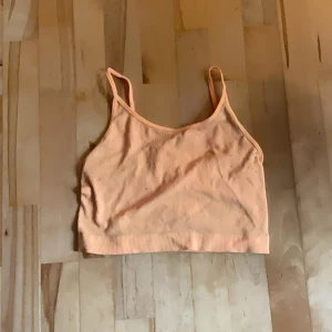 Ribbad persikofärgad linnetopp från New Yorker - Säljer en ribbad linnetopp i persikofärg med smala axelband. Toppen är croppad och materialet är mjukt och stretchigt för en bekväm känsla hela dagen. Färgen är mycket mer orange i verklighet än på bild, så lita inte på hur pastell den är på bild. Lite nopprig som syns på bild men det är lätt att dra av och det som sitter är från att den har legat med hoodies i garderoben, den är tvättad. 