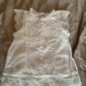 Vit spetsblus från Zara - Superfin vit blus från Zara med broderade detaljer och spets längs ärmar och nederkant. Blusen är ärmlös med volangkant. Storleken är 152 men jag är runt 162 och den passar mig som ni ser på en bild! Använt få gånger och i ett mycket bra skick!