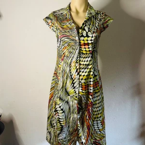 Skjortklänning från Takezo med färgsprakande retromönster Stl 38/M Vintage -  Retroinspirerad skjortklänning från Takezo i bra vintageskick. Sydd i ett mjukt polyestermaterial med lätt stretch som ger fin passform. Kort ärm, krage och knappar framtill. Det färgstarka mönstret i gult, orange, vitt och svart gör den till ett riktigt statementplagg. Storlek 38. Passar mig tyvärr inte längre.  Prutning accepteras inte, men jag erbjuder rabatt vid köp av flera plagg. Jag rensar garderoben – passa på att kika 
