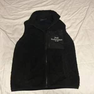 Svart fleeceväst Peak Performance M - Svart fleeceväst från Peak Performance med hög krage och dragkedja framtill. Västen har en bröstficka med logga och dragkedja, samt mjuk och fluffig yta. Perfekt lager-på-lager-plagg för kyliga dagar. Den är sällsynt för går ej att hitta på nätet nånstans
