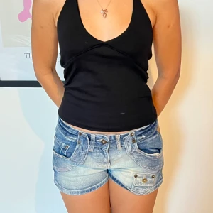 Svart halterneck topp från lager 157 - Svart halterneck topp från 157 i storlek XS. Toppen är ärmlös med djup v-ringning och knyt i nacken. Snygg croppad passform som sitter tight och är perfekt till jeans eller kjol. Mjuk och stretchig bomullskänsla.