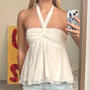 Vit halterneck topp med twistad front - Supersöt vit halterneck topp med twistad detalj framtill och flowig, luftig passform. Tunt, lätt tyg som ger en romantisk vibe och snyggt fall. Perfekt till jeans eller kjol för en fräsch look.