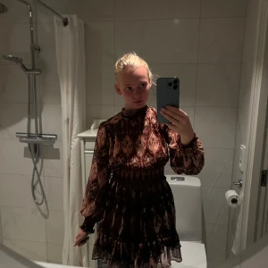 Mönstrad kortklänning med volang - Supersöt kortklänning med volangkant och långa puffärmar. Klänningen har ett brunt och vinrött mönster med inslag av beige och svart, samt smock i midjan för en snygg passform. Tunt, lätt material som känns luftigt och skönt.från Zara. Nypris 549kr