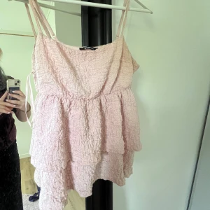 Ljusrosa volangtopp  - En ljusrosa kort blus från Gina Tricot med smala axelband och flera volanger. Toppen har en krinklad struktur och är perfekt för varma dagar med en lätt och luftig modell 