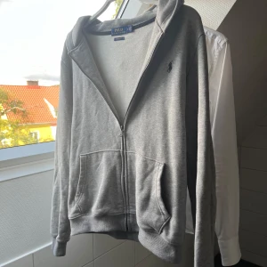 Grå Polo Ralph Lauren hoodie - ALDRIG ANVÄNT. Säljer en klassisk grå hoodie från Polo Ralph Lauren i modellen Custom Fit, storlek Medium, passar även S. Den är i mycket gott skick – inga fläckar, hål eller noppor. Mjuk och bekväm bomullsblandning, perfekt för vardagsbruk eller lager-på-lager under hösten. Diskret broderad logga på bröstet.  💨 Nypris: ca 2500 kr 🧼 Fräsch och nytvättad