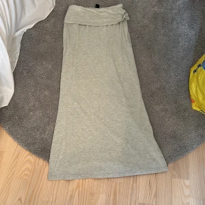 Ljusgrå långklänning i bomull - Enkel och stilren ljusgrå långklänning i mjukt bomullstyg. Klänningen har en rak passform och en bred kant upptill som kan vikas ner för en snygg detalj. Perfekt för varma dagar eller avslappnade tillfällen.