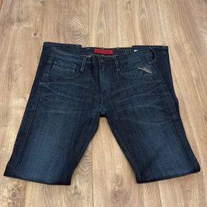 Mörkblå jeans från Replay - Snygga mörkblå jeans från Replay med klassisk femficksdesign och diskreta slitningar. Jeansen har normal passform och är tillverkade i jeansmaterial med dragkedja och knapp framtill. Perfekta för en chill och stilren look.