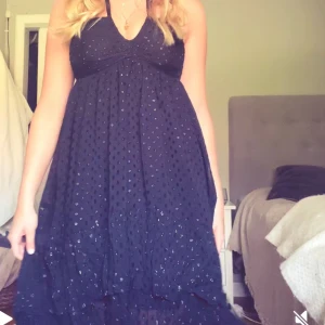 Svart prickig långklänning H&M - Supersöt svart långklänning från H&M med halterneck och v-ringning. Klänningen har ett glittrigt prickigt mönster och volangdetaljer nertill. Lätt och luftig, perfekt för sommarkvällar eller när du vill känna dig extra fin. Inga tecken på användning!