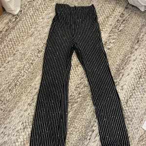 Svarta glittriga byxor Divided - Svarta bootcut byxor från Divided H&M med smala silvriga ränder och glittrig effekt. Stretchigt material 