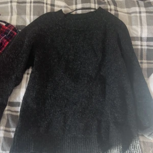 Svart stickad tröja med rund hals - Mysig svart stickad tröja med rund hals och långa ärmar. Perfekt för kyliga dagar och enkel att matcha med jeans eller kjol. Tröjan har ribbade muddar vid ärmslut och nederkant för extra komfort.