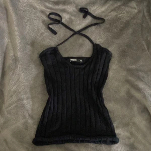 Svart ribbad linnetopp från BikBok - Säljer en svart ribbad linnetopp från BikBok i storlek XS. Toppen har smala axelband som kan knytas i nacken för en snygg halterneck-look. Materialet är mjukt och stretchigt, perfekt för att skapa en cool och enkel stil. Aldrig använd