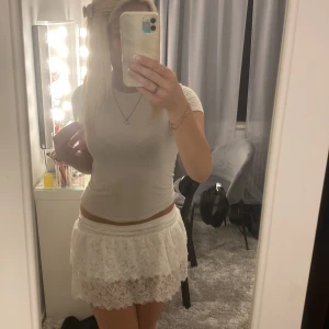 Vit spetskjol med volang - Supersöt vit kortkjol med två lager spets och volangkant. Kjolen har bred resår i midjan och är gjord i ett lätt, transparent spetsmaterial med blommigt mönster. 