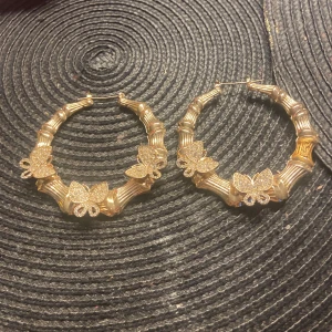 Guldiga hoop-örhängen med fjärilar - Säljer ett par stora, runda hoop-örhängen i guld med glittriga fjärilsdetaljer. 