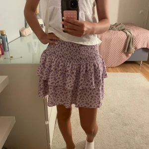 Ljuslila blommig volangkjol - Supersöt kort kjol i ljuslila med små lila blommor och volanger från Gina Tricot. Knappt använd då jag har så många kjolar. 