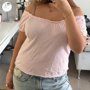 Ljusrosa offshoulder topp - Supersöt ljusrosa offshoulder topp med korta ärmar och rynkade kanter. Tunt, lätt och skrynkligt tyg som ger en avslappnad vibe. Perfekt till jeans eller kjol för en somrig look.