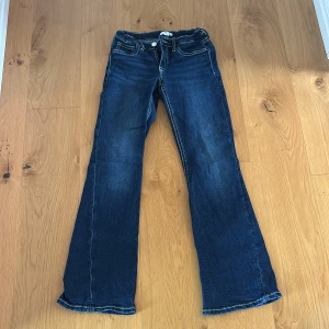 Blå bootcut jeans från Gina Tricot - Snygga blå jeans från Gina Tricot i bootcut-modell med kontrastsömmar och coola fickdetaljer bak. Klassisk femficksdesign och låg midja. Perfekta för dig som gillar en retro vibe och vill sticka ut lite extra.