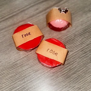 Handgjord tvål, doft av rosor - Säljer handgjorda runda tvålar med rosdoft, inslagna i plast och pappersband. Färgerna är röd och ljusrosa. Basen är från Greenum, med sheasmör och aloe vera, vegansk och återfuktande. Perfekt för dig som gillar naturliga ingredienser och mild doft.