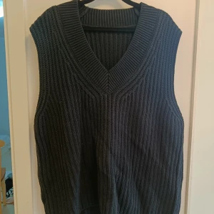 Svart stickad väst med v-ringning - Säljer en svart stickad väst med bred v-ringad hals och ribbad struktur. Västen har en loose passform och är perfekt att slänga över en skjorta eller t-shirt för en chill och stilren look. Passar dig som gillar enkla och tidlösa plagg.