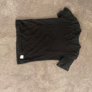 Svart v-ringad t-shirt - En enkel svart t-shirt med v-ringad hals och korta ärmar. T-shirten har en clean look utan mönster eller detaljer och är gjord i mjukt material som känns skönt mot huden. Perfekt för dig som gillar minimalistisk stil.