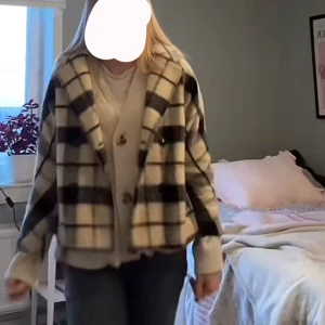 Rutig kort kappa - Säljer kort kappa i svart, grått och beige rutigt mönster. Jackan är croppad med bred krage, knappar framtill och två fickor. Perfekt för dig som vill ha en mysig och trendig look till hösten eller vintern.