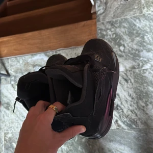 Svarta Nike Air Jordan 4 sneakers - Säljer ett par helsvarta Nike Air Jordan 4 sneakers med klassisk mesh och detaljer i mocka. Skorna har en chunky sula, snörning och ikoniska Jordan-loggan under sulan. Perfekta för dig som gillar streetstyle och vill ha en clean look.