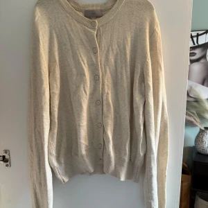 Beige kofta från H&M med knappar - Snygg beige kofta från H&M i storlek S. Den har rund hals, långa ärmar och stängs med matchande knappar framtill. Materialet är mjukt och stickat, perfekt för lager-på-lager. Passar dig som gillar enkel och clean stil.
