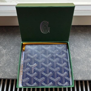 Blå plånbok med mönster - Snygg blå plånbok med ikoniska grafiska mönster i vitt och grått. Plånboken har flera kortfack och är tillverkad i skinn. Perfekt för dig som vill ha något unikt och stilrent i fickan.