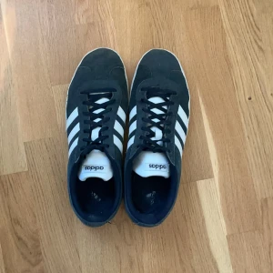 Adidas Campus sneakers i mörkblå mocka - Snygga Adidas Campus sneakers i mörkblå mocka med klassiska vita ränder på sidorna och vit sula. Skorna har rund tå, snörning och låg profil. Perfekta för en avslappnad streetstyle-look.
