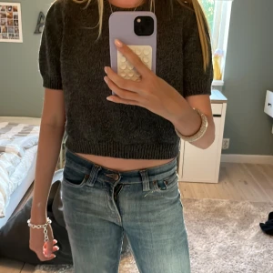 stickad T-shirt - Säljer en mörkgrå croppad stickad tröja från Zara med korta ärmar och rund hals. Tröjan har ribbade muddar vid ärmslut och nederkant, vilket ger en snygg och chill vibe. Perfekt att matcha med jeans eller kjol för en trendig look. Andvänd fåtal gånger.