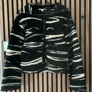 teddyjacka  - Säljer en svart och vit teddyjacka med zebramönster och dragkedja framtill. Jackan är långärmad, perfekt för dig som vill sticka ut med en cool och mysig stil. Passformen är normal och materialet är fluffigt och mjukt.