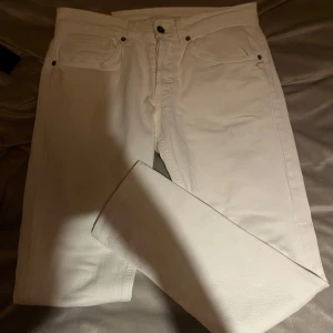 Vita jeansbyxor från dondup - Säljer ett par stilrena vita jeansbyxor från Gucci med klassisk femficksdesign och diskret logga på bakfickan. Byxorna har raka ben och är tillverkade i mjuk bomull för en clean look. Perfekta för dig som vill sticka ut med en lyxig touch.