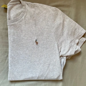 Beige t-shirt Polo Ralph Lauren - Snygg beige t-shirt från Polo Ralph Lauren i bomull med klassisk rund hals och broderad logga på bröstet. Modellen är slim fit och har korta ärmar. Perfekt för en clean och stilren look.