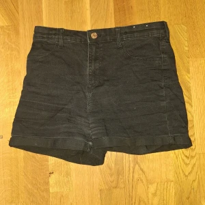 Svarta högmidjade jeansshorts &Denim - Svarta jeansshorts från &Denim med hög midja och klassisk femficksdesign. Modellen har uppvikta benslut och knappstängning fram. Materialet är slitstarkt denim som ger en cool och enkel vibe. Perfekt för dig som gillar stilrena och tidlösa plagg.