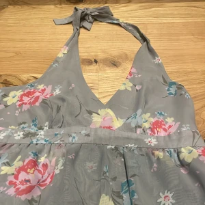 Grå blommig kortklänning med volanger - Supersöt grå kortklänning med blommigt mönster i rosa, blått och gult. Klänningen har omlott-v-ringad hals, knyt i nacken och flera lager volanger nedtill. Perfekt för sommarens alla tillfällen! Materialet känns lätt och luftigt. Från Lindex i storlek 40, säljer då den tyvärr är för stor för mig❤️
