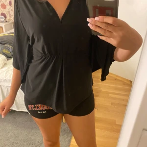 Svart blus med knyt från Mississippi Paris - Snygg svart blus från Mississippi Paris med v-ringning och trekvartsärmar. Blusen har en markerad midja och knytband i ryggen för extra detalj. Luftigt material som ger en skön och avslappnad känsla. Perfekt till jeans eller kjol.