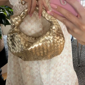 Guldig väska  - Superfin handväska i guldigt skinn med flätad design och rundad form. Bottega liknande