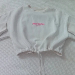 Vit croppad Juicy Couture sweatshirt - Säljer en vit sweatshirt från Juicy Couture i storlek XS. Den har en snygg croppad passform med snörning i nederkant och rosa tryck med texten juicy både fram och bak. Mjuk bomullskvalitet och perfekt för en chill och avslappnad vibe. Tröjan är i mycket bra skick.