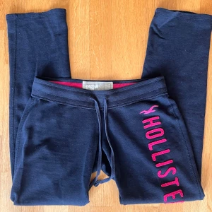  Hollister mjukisbyxor - Mörkblå  lågmidjade mjukisbyxor från Hollister med rosa broderad logga längs benet. Verkligen jätte fina men för korta för mig som är 180. Slitna vid benslutet se sista bild. De är i ett användt skick men inga tydliga defekter.