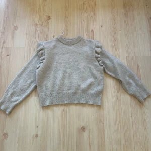 Grå stickad tröja med volang Gina Tricot - Superfin grå stickad tröja från Gina Tricot med volangdetaljer på axlarna. Tröjan har rund hals, ribbade muddar och lång ärm. Perfekt för dig som gillar en enkel men ändå söt look med extra detaljer på axlarna. Storlek 146/152! Säljer då den inte används