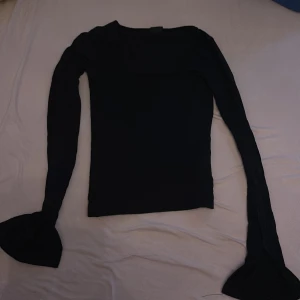 Svart långärmad topp med utsvängda ärmar - Snygg svart långärmad topp med tight passform och unika utsvängda ärmslut. Enkel och stilren design som passar perfekt till jeans eller kjol. Mjuk och stretchig känsla, perfekt för dig som gillar minimalistisk stil.