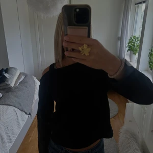 Svart offshoulder tröja - Svart långärmad tröja med offshoulder-design och en cool axelrem på ena sidan. Tröjan är i mjuk bomull och har en relaxed fit som passar perfekt till jeans. Enkel men ändå unik detalj som gör outfiten extra snygg!