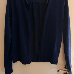 Mörkblå kofta från LOFT, storlek M - Mörkblå kofta från LOFT i storlek M. Klassisk modell med långa ärmar och knappar framtill. Tunn och mjuk, perfekt att slänga över en t-shirt eller linne. Enkel och stilren design som funkar till det mesta.